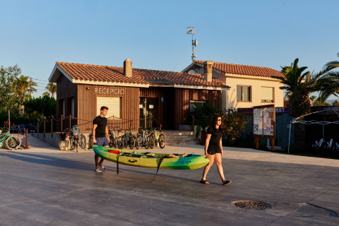 Dos personas llevan un kayak frente a la recepción del parque vacacional TAIGA Delta de l'Ebre en Cataluña, España.