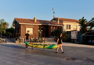 Dos personas llevan un kayak frente a la recepción del parque vacacional TAIGA Delta de l'Ebre en Cataluña, España.