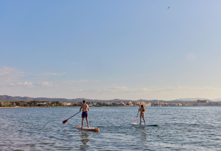 Two people paddleboarding near TAIGA Delta de l'Ebre holiday park in Catalonia, Spain, with a scenic view.