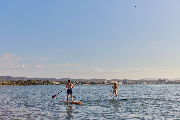 Twee mensen suppen bij het TAIGA Delta de l'Ebre vakantiepark in Catalonië, Spanje, met uitzicht op de kust.
