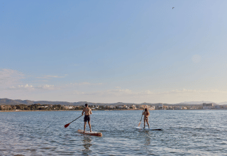 Zwei Personen paddeln stehend auf Boards vor dem TAIGA Delta de l'Ebre Ferienpark in Katalonien, Spanien.