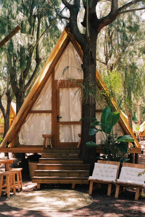 Dreieckige Holzhütte bei TAIGA Tarifa, Andalusien, Spanien, mit Sitzgelegenheiten im Freien und umliegenden Bäumen.