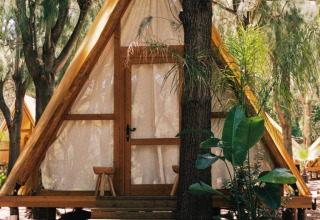 A-frame wooden cabin at TAIGA Tarifa holiday park in Andalusia, Spain, surrounded by trees and outdoor seating.
