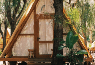 A-vormige houten hut bij TAIGA Tarifa vakantiepark in Andalusië, Spanje, omgeven door bomen en buitenzitjes.