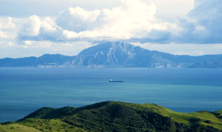 Uitzicht op de blauwe zee vanaf groene heuvels bij Tarifa, Cádiz, met bergen op de achtergrond.