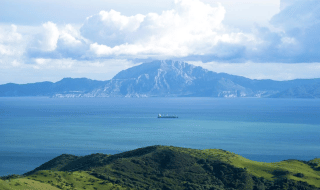 Vista del mar azul desde las colinas verdes cercanas a Tarifa, Cádiz, con una cordillera al fondo.