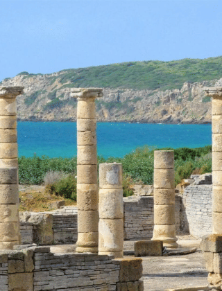 Ruinas de columnas antiguas y una estatua junto al mar en Tarifa, Cádiz, Andalucía, España, con colinas verdes.