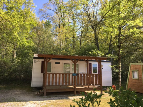 Bungalow Larraun cabin nestled among lush green trees, wooden porch, peaceful nature, blue sky above.