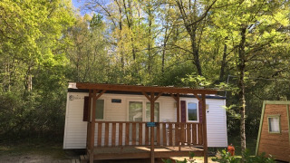 Bungalow Larraun cabin nestled among lush green trees, wooden porch, peaceful nature, blue sky above.