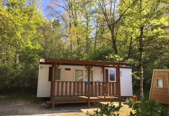 Bungalow Larraun cabin nestled among lush green trees, wooden porch, peaceful nature, blue sky above.