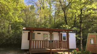 Cabaña Bungalow Larraun rodeada de árboles verdes y naturaleza, con un porche de madera bajo cielo azul.