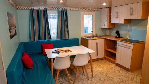 Interior of Bungalow Larraun at Camping Etxarri in Spain, featuring blue seating, dining table, and kitchenette.