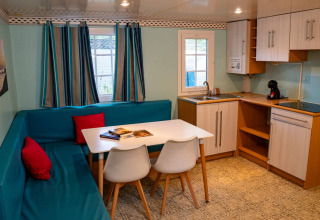 Interior del Bungalow Larraun en Camping Etxarri, España, con sofá azul, mesa comedor y cocina equipada.