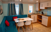 Interior del Bungalow Larraun en Camping Etxarri, España, con sofá azul, mesa comedor y cocina equipada.