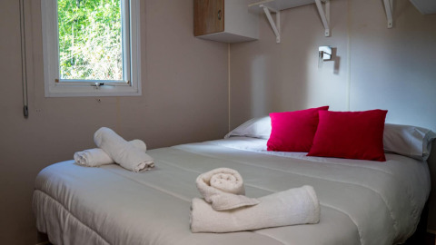 Accogliente camera da letto nel Bungalow Larraun al Camping Etxarri in Spagna, con cuscini rossi e asciugamani arrotolati.