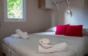 Cozy bedroom in Bungalow Larraun at Camping Etxarri in Spain, featuring red pillows and neatly rolled towels.