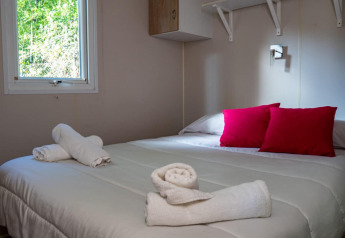 Accogliente camera da letto nel Bungalow Larraun al Camping Etxarri in Spagna, con cuscini rossi e asciugamani arrotolati.