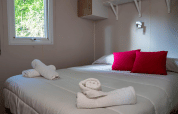 Acogedor dormitorio en el Bungalow Larraun del Camping Etxarri en España, con cojines rojos y toallas enrolladas.