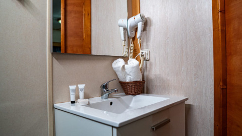 Bathroom in Bungalow Larraun at Camping Etxarri, Spain, with sink, mirror, hairdryers, and rolled towels.