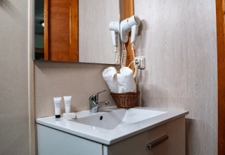 Bathroom in Bungalow Larraun at Camping Etxarri, Spain, with sink, mirror, hairdryers, and rolled towels.