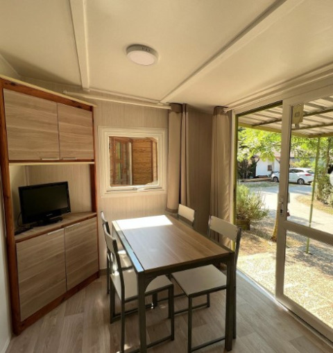 Interno luminoso del Bungalow Urbasa con tavolo da pranzo, sedie, piccolo TV e vista sul verde esterno.