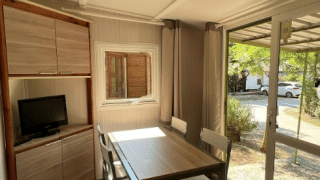Bright interior at Bungalow Urbasa with dining table, chairs, small TV, and view of greenery outside.