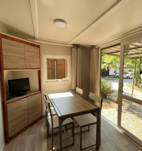 Interior luminoso en Bungalow Urbasa con mesa de comedor, sillas, televisor y vista al exterior natural.