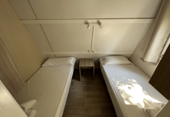 Due letti singoli nel Bungalow Urbasa al Camping Etxarri in Spagna, con comodino e arredo luminoso.