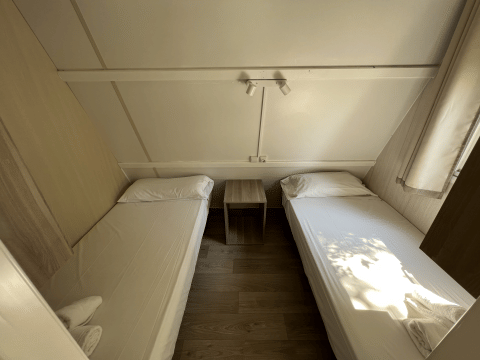 Dos camas individuales en el Bungalow Urbasa en Camping Etxarri, España, con mesita y decoración luminosa.