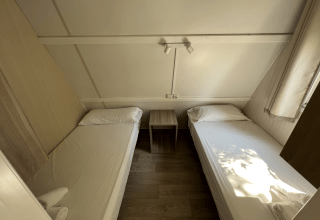 Dos camas individuales en el Bungalow Urbasa en Camping Etxarri, España, con mesita y decoración luminosa.