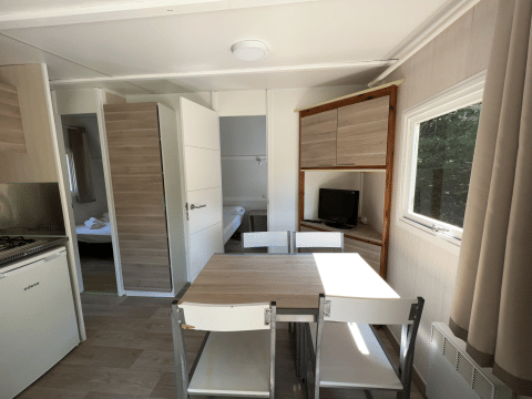 Bright interior of Bungalow Urbasa with dining table, chairs, kitchen, and TV at Camping Etxarri, Spain.