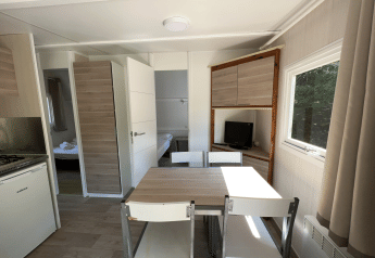 Interno luminoso del Bungalow Urbasa con tavolo, sedie, cucina e TV al Camping Etxarri, Spagna.