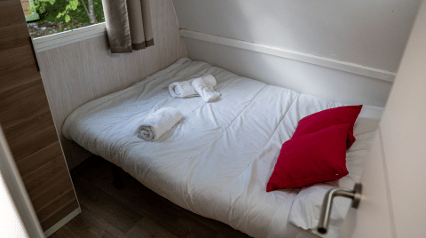 Bedroom inside Bungalow Urbasa at Camping Etxarri, Spain, featuring a bed, red pillows, and rolled towels.