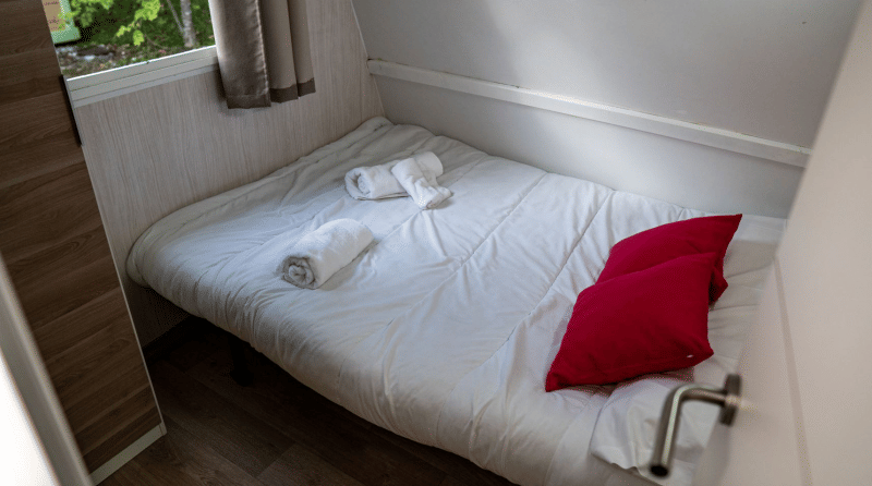 Dormitorio en Bungalow Urbasa de Camping Etxarri, España, con cama, cojines rojos y toallas dobladas.