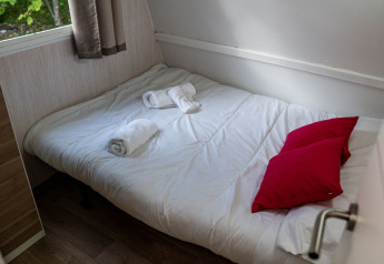 Chambre du Bungalow Urbasa au Camping Etxarri en Espagne avec lit, coussins rouges et serviettes roulées.