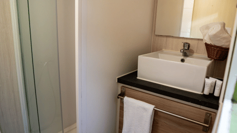 Compact bathroom in Bungalow Urbasa, Camping Etxarri, Spain, featuring square sink, mirror, and shower area.