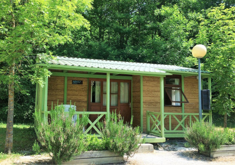 A cozy cabin called Bungalow Aratz, set amidst greenery with a porch, outdoor seating, and lush trees.