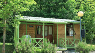 Accogliente bungalow in legno chiamato Aratz, immerso nel verde con veranda e sedie da esterno.