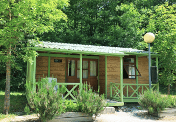 Accogliente bungalow in legno chiamato Aratz, immerso nel verde con veranda e sedie da esterno.