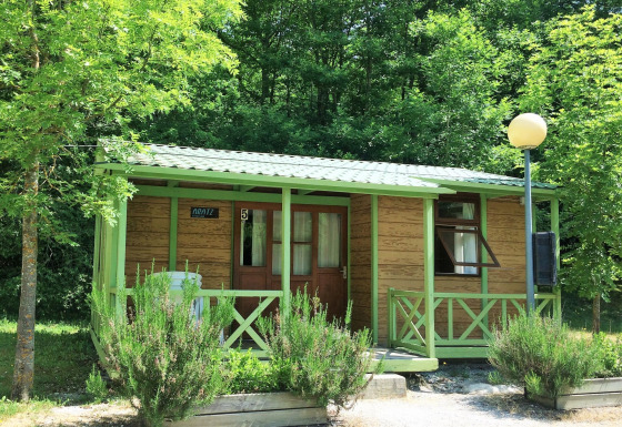 Acogedora cabaña llamada Bungalow Aratz rodeada de naturaleza, árboles y un pequeño porche delantero.