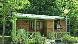 Acogedora cabaña llamada Bungalow Aratz rodeada de naturaleza, árboles y un pequeño porche delantero.