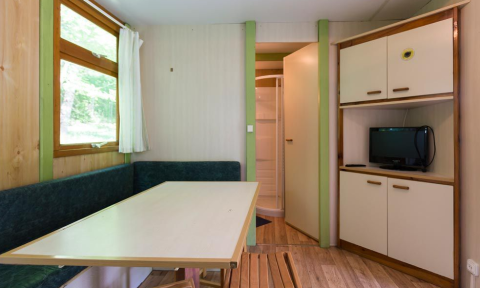 Interior of Bungalow Aratz at Camping Etxarri in Spain showing a table, bench seating, small TV, and bathroom.