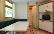 Interior of Bungalow Aratz at Camping Etxarri in Spain showing a table, bench seating, small TV, and bathroom.