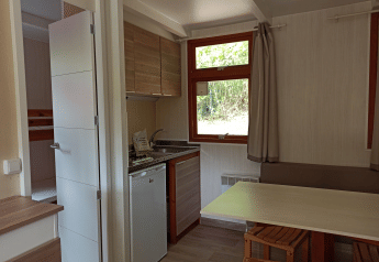 Interior del Bungalow Aratz en Camping Etxarri, España, con cocina, mesa de comedor y ventana al exterior.