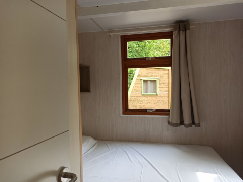 Interior view of Bungalow Aratz at Camping Etxarri in Spain, showing a bed and window facing another cabin.
