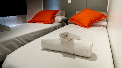 Deux lits simples avec draps blancs, coussins orange et serviettes propres au Mobile home Urederra, Camping Etxarri, Espagne.