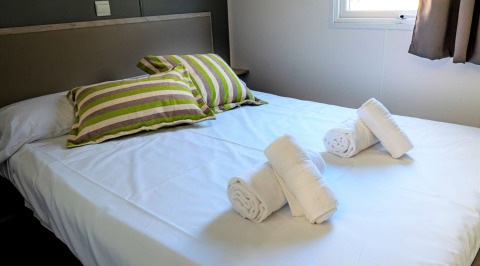 Camera da letto nel Mobile home Urederra al Camping Etxarri in Spagna con letto rifatto e asciugamani arrotolati.