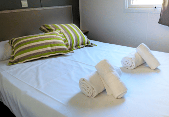 Bedroom in Mobile home Urederra at Camping Etxarri, Spain, with a made bed and rolled towels on top.