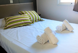 Dormitorio en Mobile home Urederra en Camping Etxarri, España, con la cama hecha y toallas enrolladas.