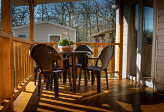 Sonnige Terrasse beim Mobile Home Urederra am Camping Etxarri in Spanien mit Plastikmöbeln und Holzboden.